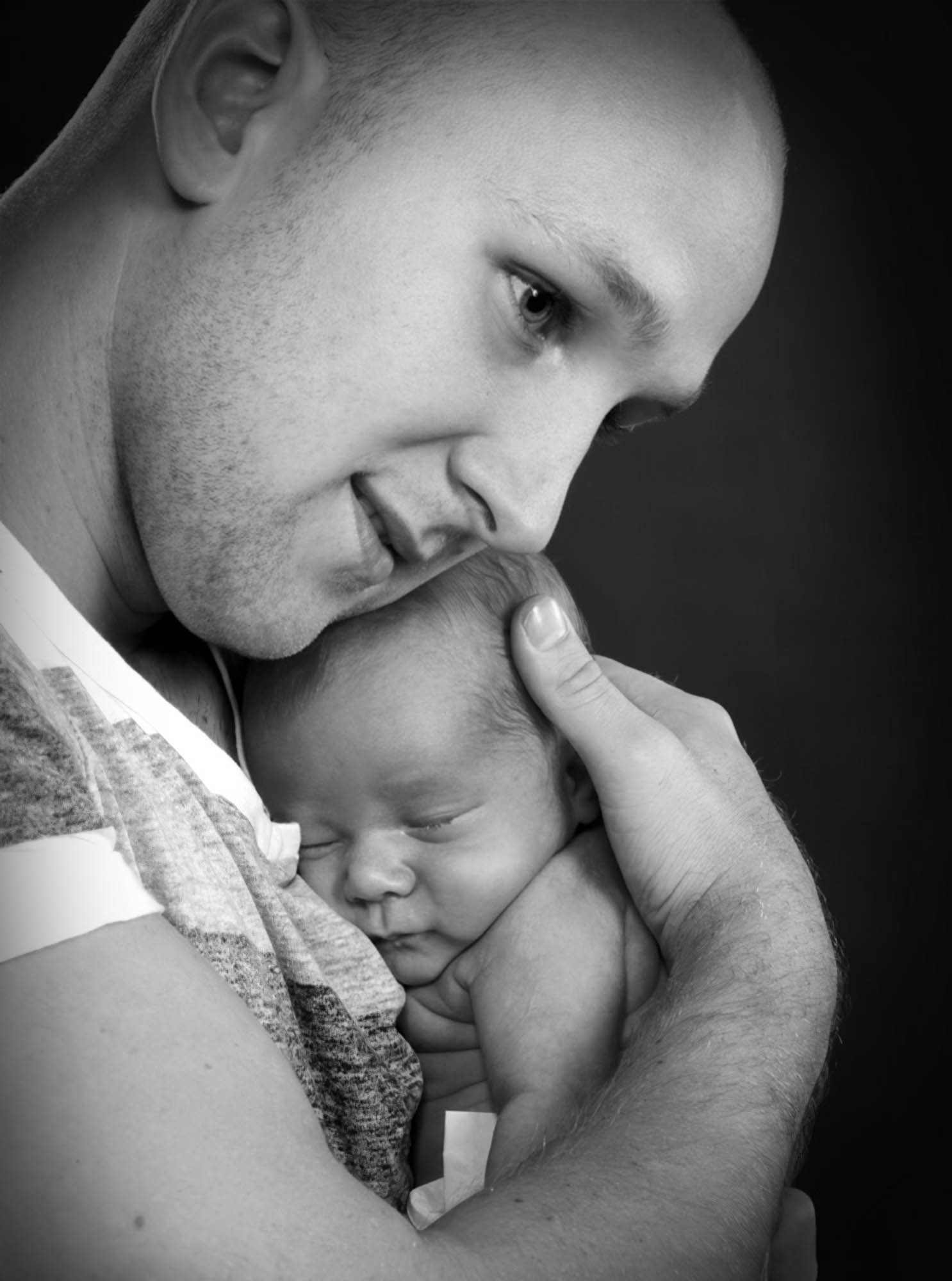 Far holder sovende nyfødt baby tæt ind til sig i et roligt sort-hvidt portræt