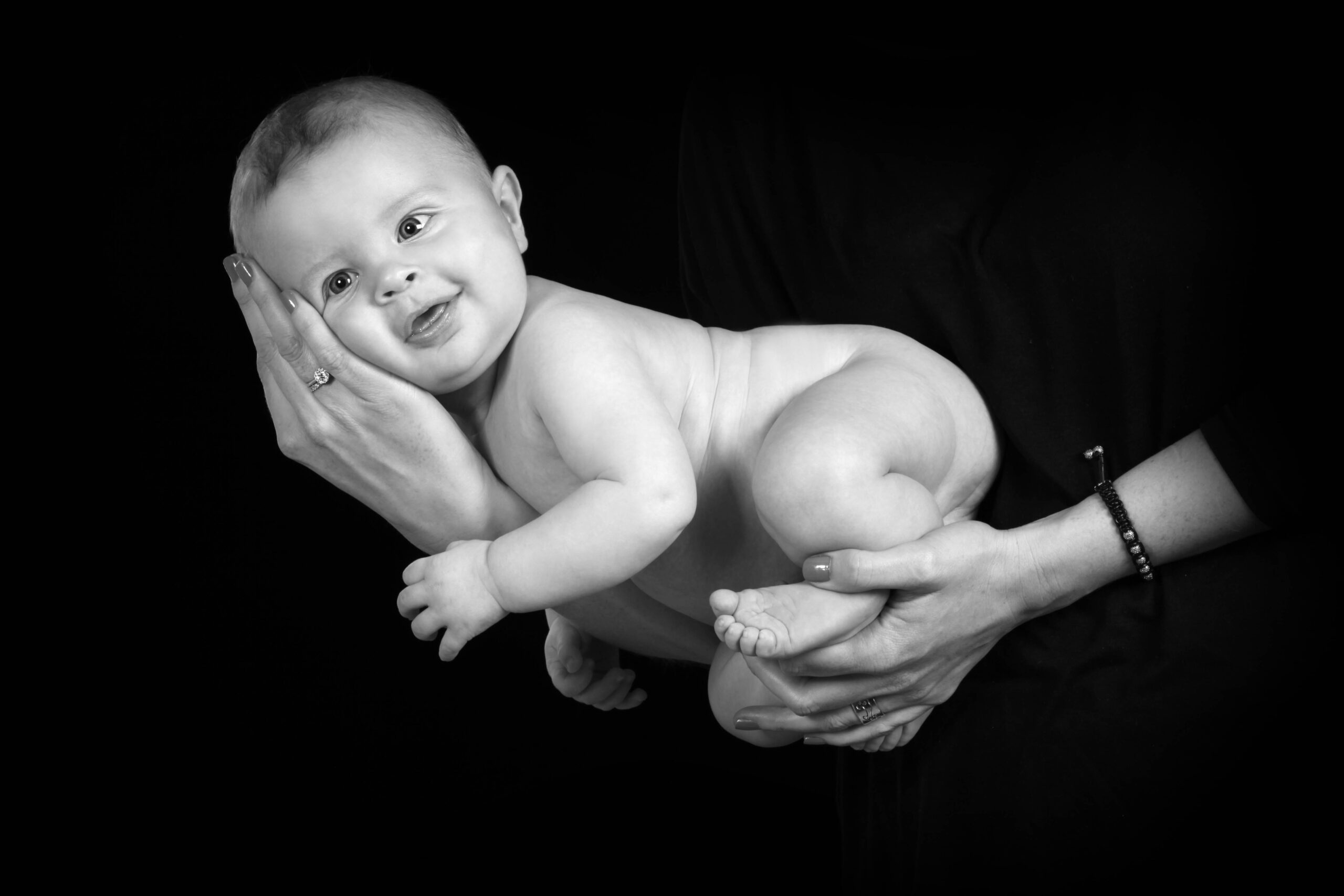 Glad baby holdt nænsomt i mors hænder mod mørk baggrund