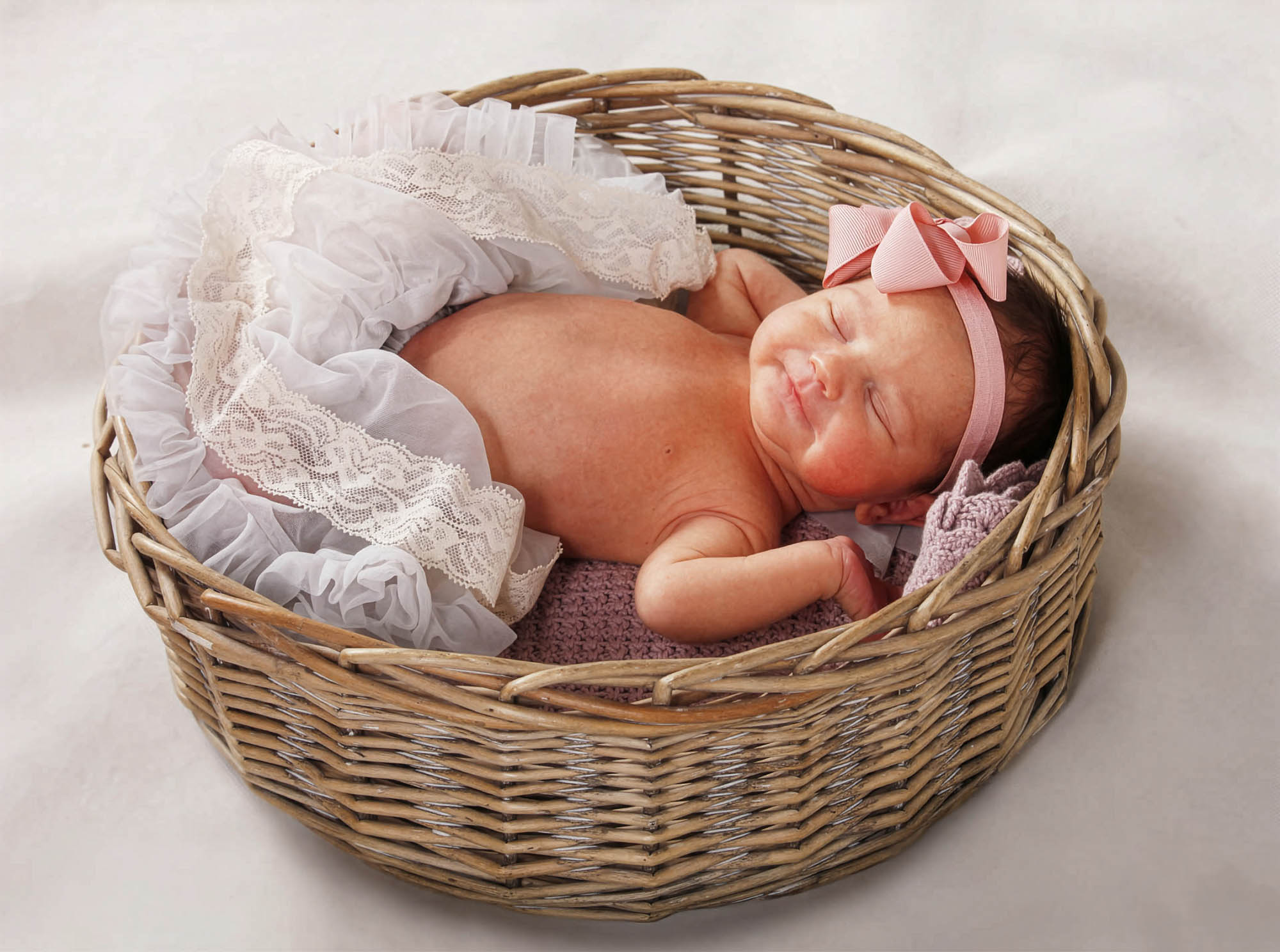 Nyfødt pige med lyserød sløjfe ligger roligt i flettet kurv