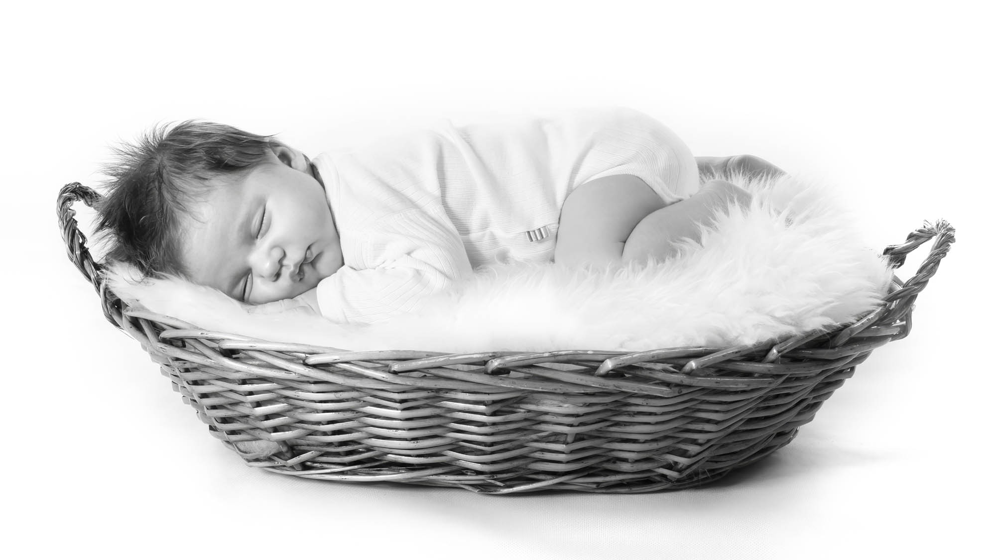 Sovende nyfødt baby i flettet kurv fotograferet i enkel og rolig studieopstilling